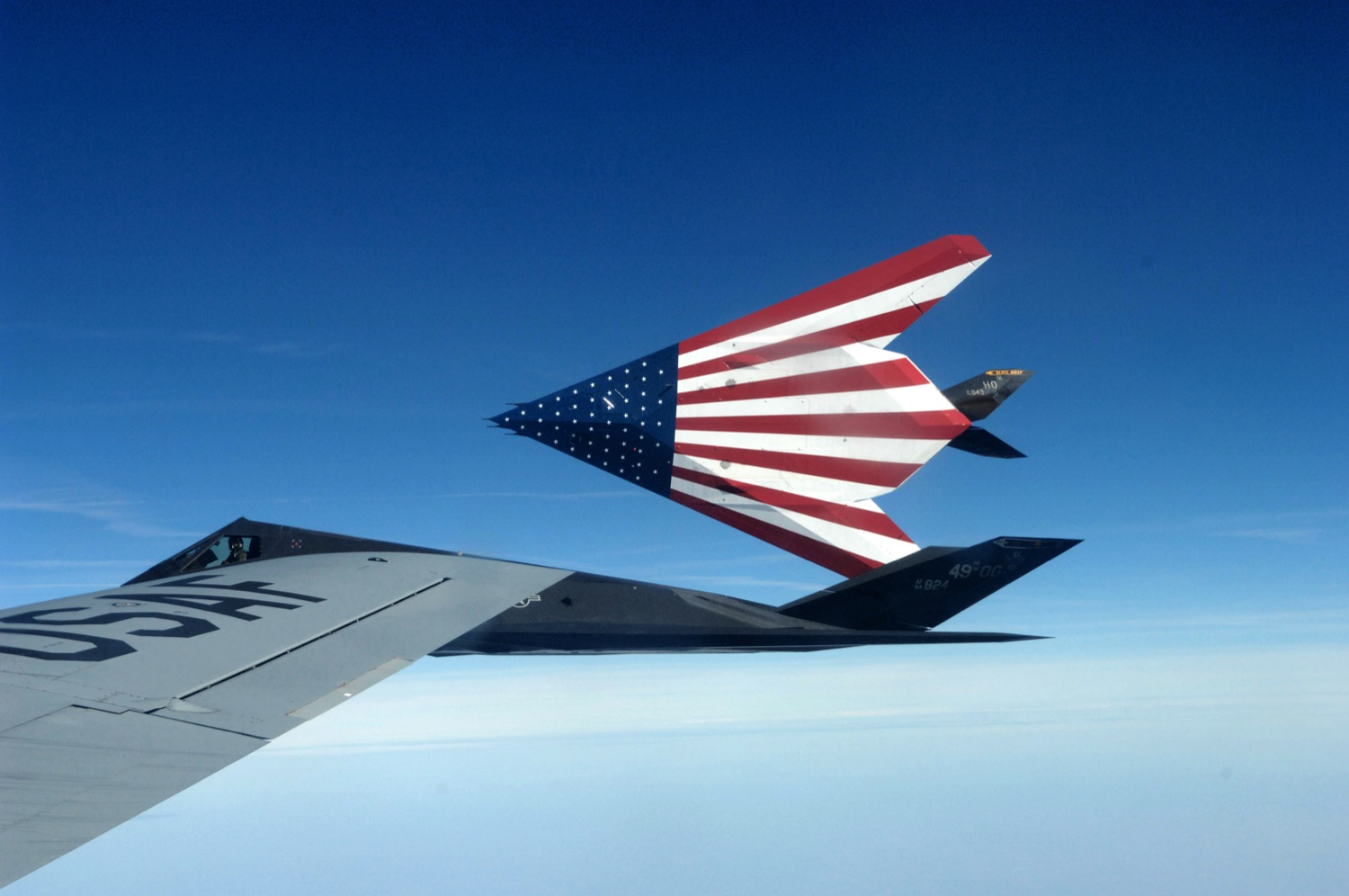 Two specially-painted F-117 Nighthawk stealth attack aircraft break away after their final aerial refueling, photographed from above with the dark faceted matte-black silhouettes against patchy clouds, March 2008 retirement mission.